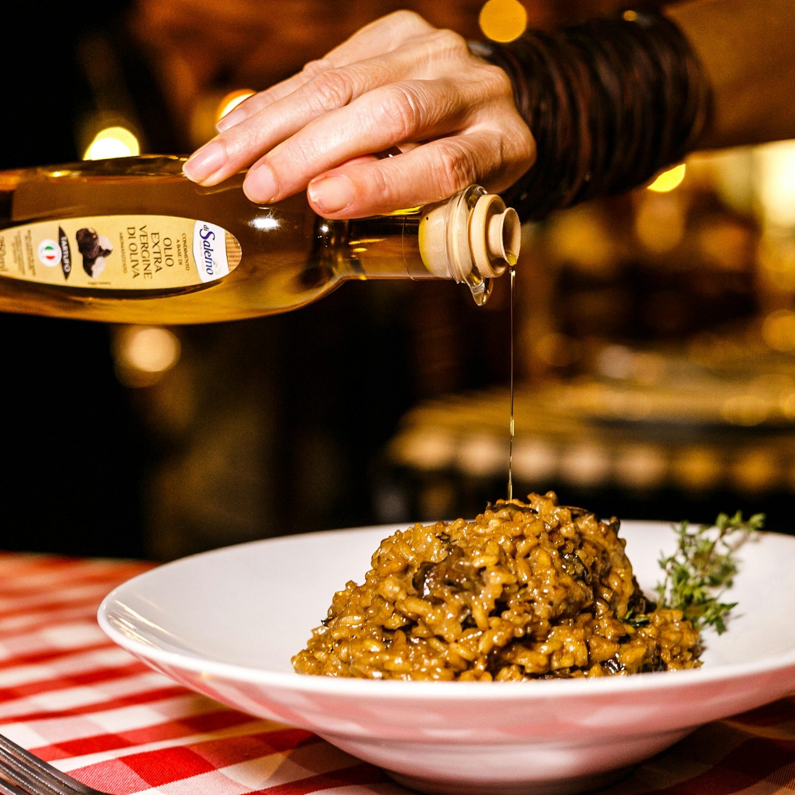 Close-up of gourmet risotto being drizzled with olive oil in an Italian restaurant setting.