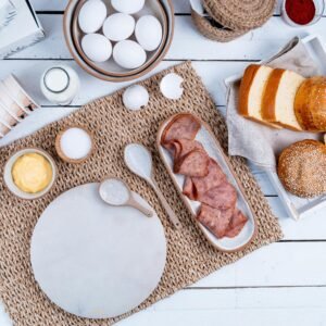 Aerial view of a rustic breakfast setting with sliced bread, ham, and eggs on a woven mat.